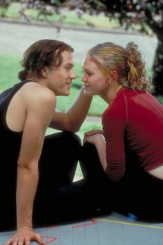 a young man and woman sitting on the ground next to each other looking at each other