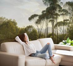 a woman sitting on top of a white couch in front of a forest wall mural