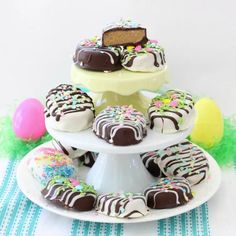 several chocolate covered desserts are stacked on a cake stand with easter eggs in the background