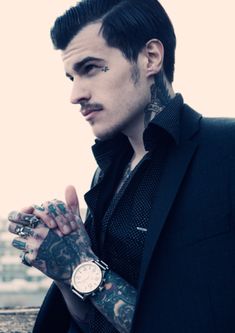 a man with tattoos on his arm and wrist standing next to a railing looking off into the distance