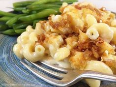 a blue plate topped with macaroni and cheese covered in sauce next to green beans