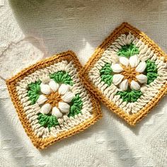 two square crocheted coasters with white and green flowers on them sitting on a table