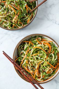 two bowls filled with veggies and chopsticks next to each other on a marble surface