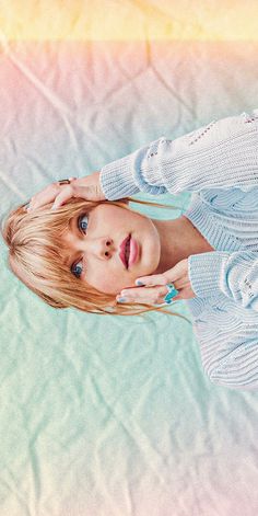 a woman with blonde hair and blue eyes poses for a photo in front of a pastel background