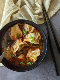 a black bowl filled with dumplings next to chopsticks