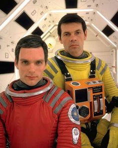 two men in space suits are holding an old fashioned camera and looking at the camera