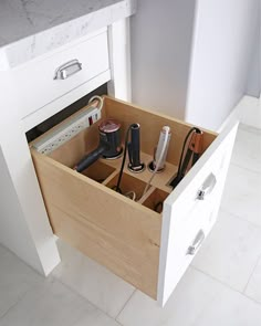 an open drawer in a kitchen with hair dryers and other items inside it on the counter