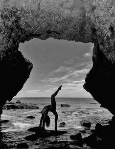 a person doing a handstand on the beach in front of some rocks and water