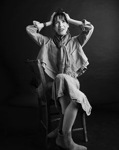 a black and white photo of a woman sitting in a chair with her hands on her head