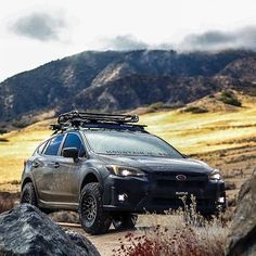 a grey suv parked on the side of a dirt road with mountains in the background