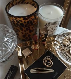 an assortment of beauty products on a table next to a candle and some glass containers