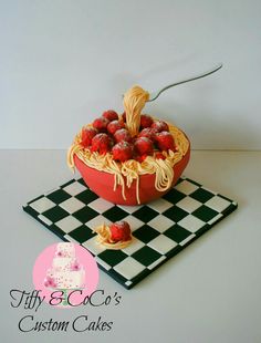 a cake shaped like a bowl of spaghetti and strawberries on a checkered tablecloth