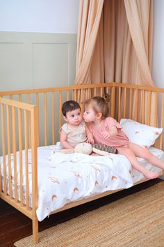 two small children sitting on top of a crib next to each other in a room