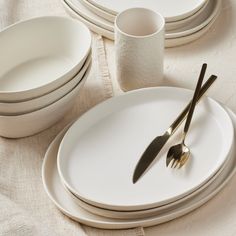 white plates and silverware are arranged on a linen tablecloth with gold - plated utensils