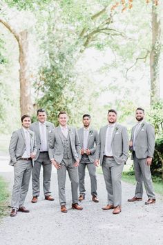 a group of men in suits standing next to each other on a dirt road near trees