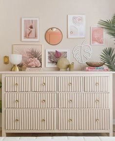 a white dresser topped with lots of pictures next to a palm tree and potted plant