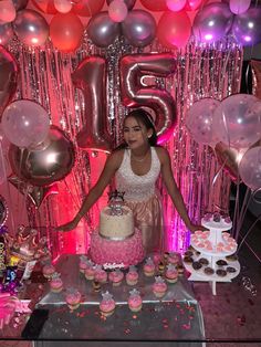 a woman standing in front of a cake and cupcakes on a table with balloons