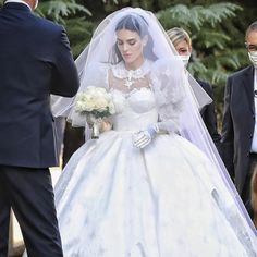 the bride is walking down the aisle with her groom wearing masks on their faces as they are surrounded by other people