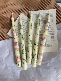 four candles with floral designs on them sitting next to an open book and some paper