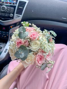 a bouquet of flowers is being held by a woman in a pink dress while sitting in the driver's seat of a car