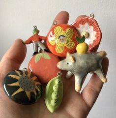 a hand is holding several ceramic ornaments in different shapes and sizes, including an orange one