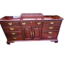 a wooden dresser with drawers and gold trimmings on the top, against a white background