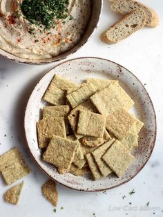 crackers and hummus on a plate next to a bowl of hummus