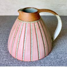 a pink and white striped vase sitting on top of a table next to a wall