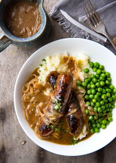 two sausages, mashed potatoes and peas on a plate with gravy