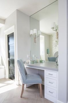 a white desk with a blue chair in front of it and a mirror on the wall