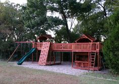 a wooden play set in the middle of a park with slide and climbing equipment on it