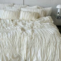 an unmade bed with white ruffled sheets and pillowcases on top of it