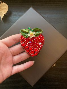 a hand holding a strawberry shaped brooch on top of a table