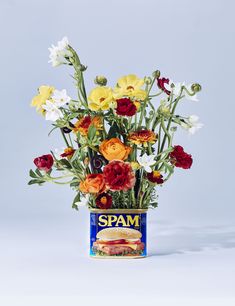 a can filled with flowers sitting on top of a white table next to a blue wall