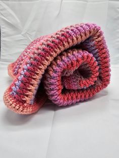 a crocheted blanket laying on top of a white bed next to a pillow