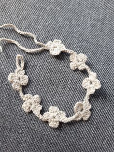 a crocheted bracelet is laying on a gray surface with white thread and beads