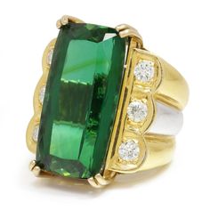 Description: This exotic green natural tourmaline gem commands a strong presence in its 18kt two-tone gold diamond-encrusted setting. The rectangular cut stone weighs approximately 22 carats and exhibits a vivid and vibrant green that ranges from very dark to bright light depending on your twist and turns. There are 3 brilliant naturals diamonds set on each side of the centerpiece weighing 1.00 carats total. The two-tone setting is a size 7 and weighs a hefty 20.4 grams. It is pre-owned and in E