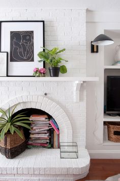 a white brick fireplace with plants and pictures on it