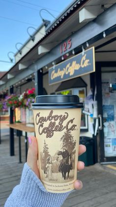 a person holding up a cup of coffee in front of a building with signs on it