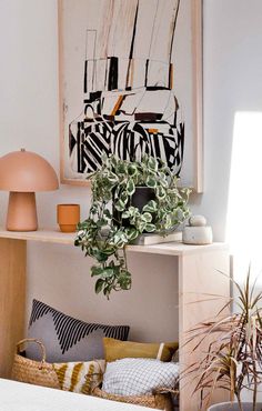 a bedroom with plants and pillows on the shelf in front of the bed, next to a painting