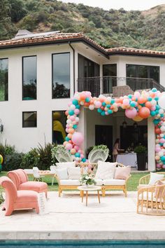 an outdoor party with balloons and couches in front of a large white house on a hill