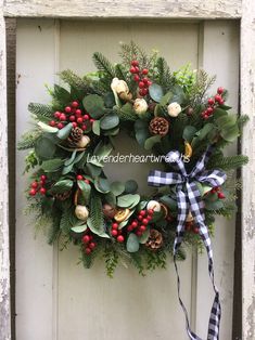 a wreath with berries, holly and pine cones hanging on a door