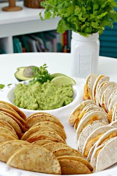 a white plate topped with tortillas and guacamole next to a bowl of guacamole