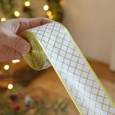 a hand holding a gold and white ribbon in front of a christmas tree