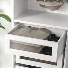 an open drawer in a white cabinet next to a potted plant and pillow on the floor