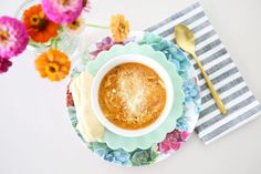 a bowl of soup on a plate with flowers and a spoon next to it,