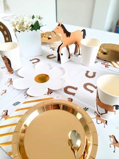 the table is set with gold and white plates, cups, and utensils