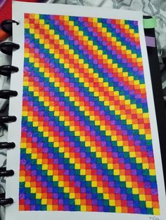 an open spiral notebook with colored squares on the cover and black markers in front of it