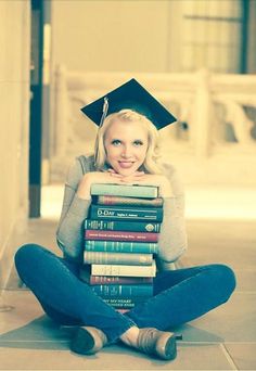 a woman sitting on the floor with her legs crossed and holding a stack of books