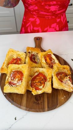 a wooden plate topped with mini pizzas on top of a white table next to a red dress